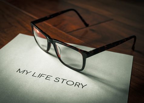 My life story wording printed on a sheet of paper sitting on a walnut floor highlighted with sunlight and a pair of spectacles in background in shallow depth of field